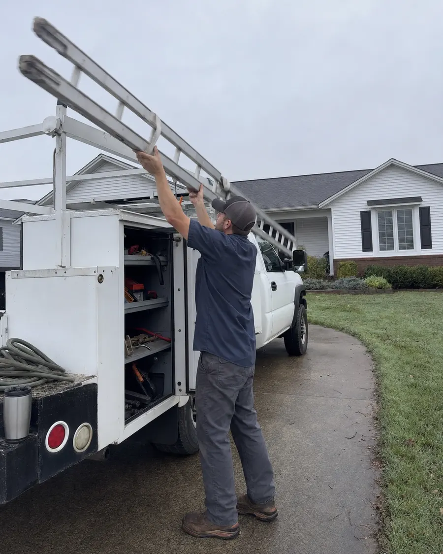 A technician lifting an extension ladder off a service truck outside a home.